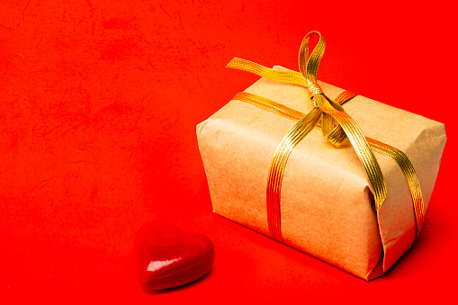 View of red gift box with ribbon an object in heart shape over red color background isolated.IMAGE MADE IN STUDIO AS CONCEPTUAL IMAGE FOR VALENTINE'S DAY