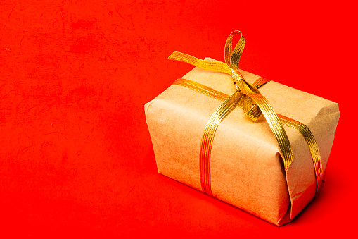 A red gift box with a gold ribbon on a gray background. The concept of holiday photography. Surprise for Valentine's Day, birthday, wedding. Copy space and front view.