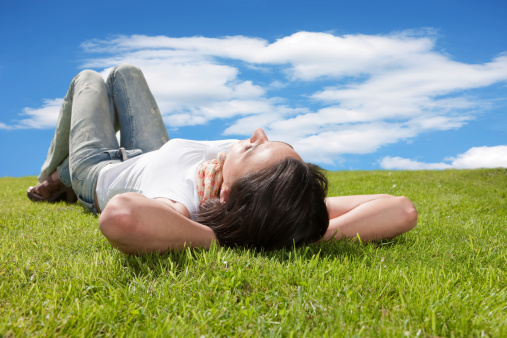 Girl resting on grass on a sunny day. Wearing a Tshirt and Jeans.