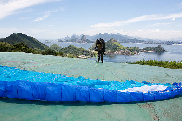 A man enjoying an exhilarating paragliding flight over Rio de Janeiro on a bright, sunny day. The vibrant cityscape and stunning coastline serve as a breathtaking backdrop as he soars through the clear blue sky, capturing the thrill of adventure and the beauty of outdoor recreation.