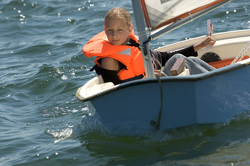 Teenage girl with life jacket sailing in small sailing vessel.