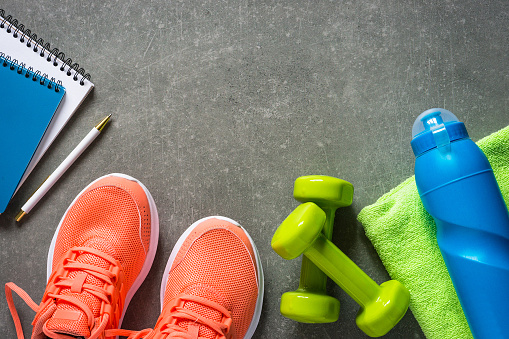 Fitness equipment. Sneakers, dumbbell, towel and bottle of water. Trayning, workout and fitness concept. Flat lay image on stone background with copy space.