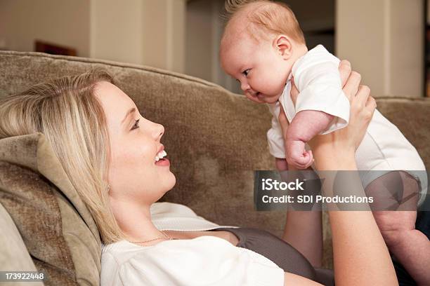 Mãe Segurando Seu Bebê Menina Pôr Em Um Sofá - Fotografias de stock e mais imagens de Abraçar - Abraçar, Adulto, Alegria