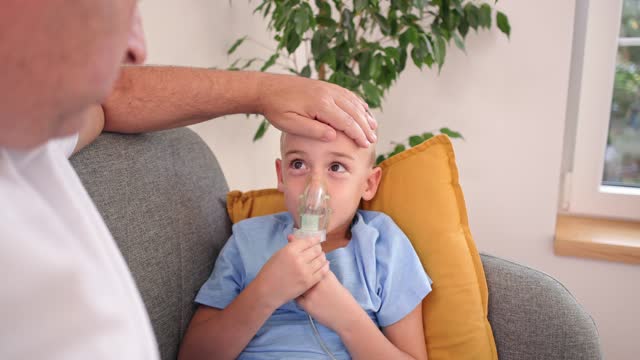 Caucasian father taking care of his asthmatic son, during his home treatment with nebulizer