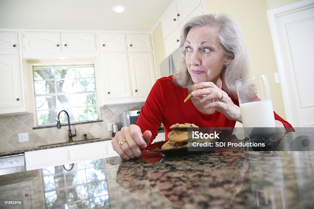 Senior adulte femme porter au quotidien des Cookies et du lait dans la cuisine - Photo de Biscuit libre de droits
