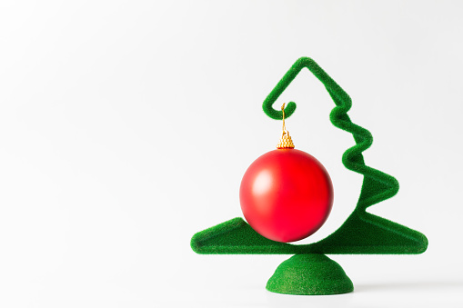 A small green Christmas tree with a hanging red ball on a white background, banner, copy space. New Year and Christmas card
