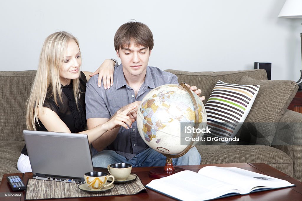 Planning a vacation A young couple are planning a vacation, looking at a globe and referring to a laptop and a book. Home interior shot. Couple - Relationship Stock Photo