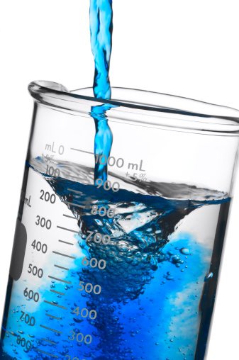 A researcher adds a blue solution to a beaker.  Isolated on White.