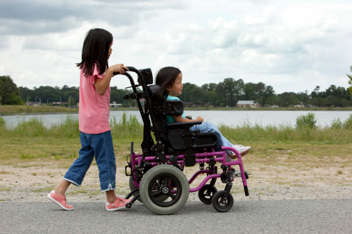 Little girl pushing her sister's wheelchair at the park. Please view these along with all