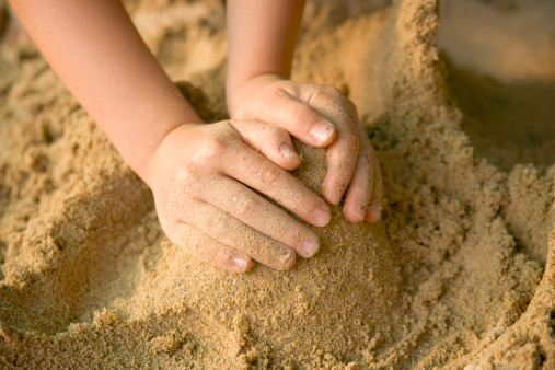 A child is forming a cone shape out of sand.