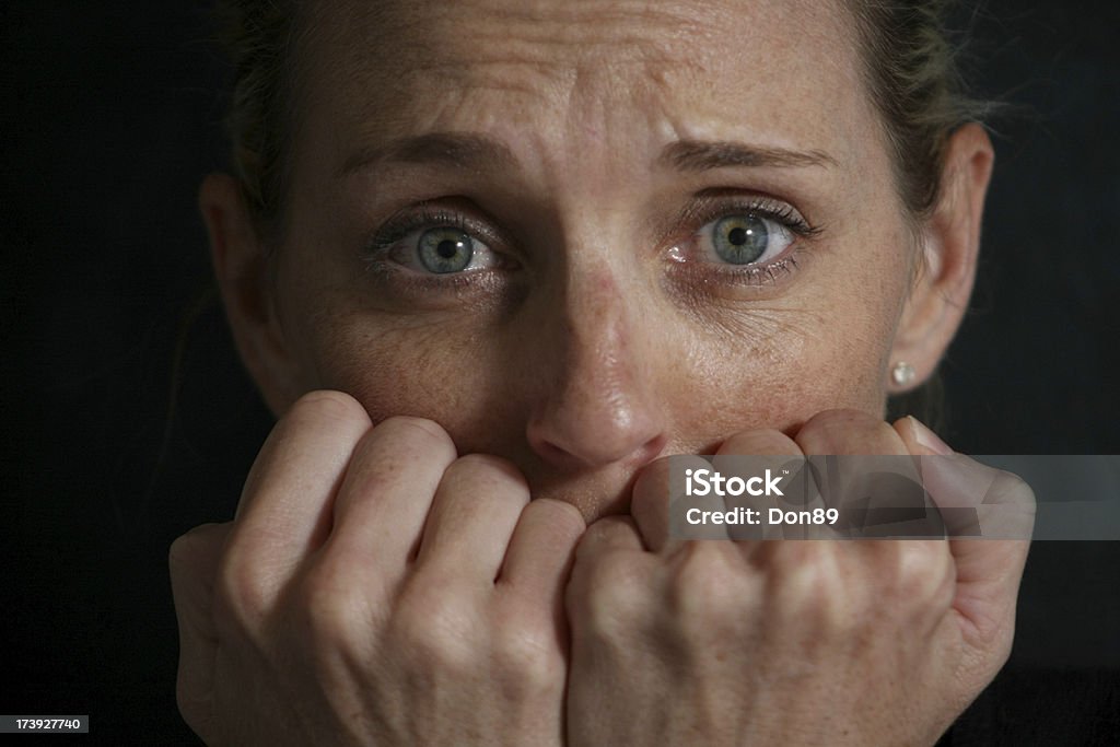 Anxiety A young caucasian woman expressing fear and anxiety with her white knuckles covering her mouth shot against a black background Butterflies in the Stomach Stock Photo