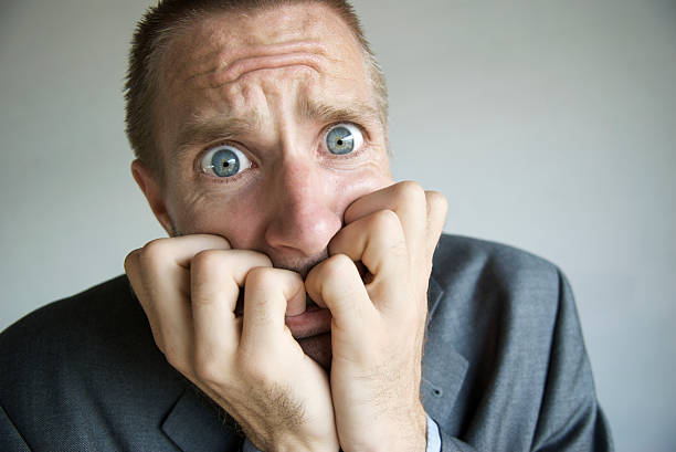 Stressed Businessman with Wide Eyes Looking Frightened Businessman with hands in his mouth looks at the camera with frightened wide eyes biting lip funny stock pictures, royalty-free photos & images