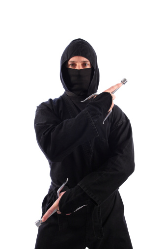 A ninja on a white background stands ready with a pair of martial arts weapons known as sais.