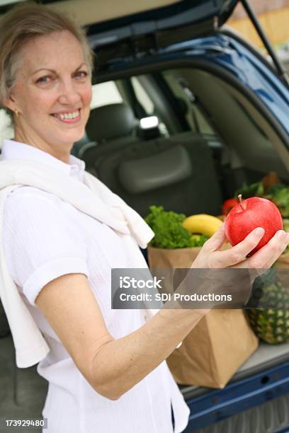 Starszy Dorosły Kobieta Trzymając Fresh Apple W Bagażnik - zdjęcia stockowe i więcej obrazów 50-59 lat