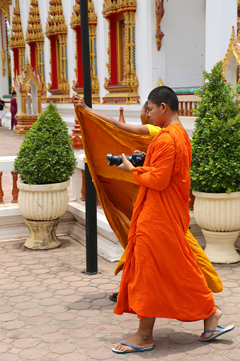 Phuket, Thailand-April 07,2016:Young Monk with Traditional Orange outfit walking with a Camera at the Temple