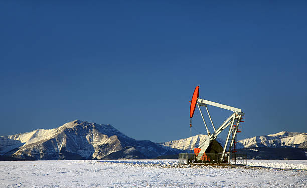 Red Pumpjack in Winter Alberta A red pumpjack against the Rockies. Near Turner Valley, Alberta, Canada. The oil and gas industry is a significant component to the Alberta economy. Oil was discovered in southern Alberta in the 1920s and has become one of the biggest industries in the western Canadian provinces. Uses for this image include industry, geology, engineering, automobile industry, gas, oil, crude, manufacturing, drilling, and fossil fuel. Nobody is in the image.  oil pump oil industry alberta equipment stock pictures, royalty-free photos & images
