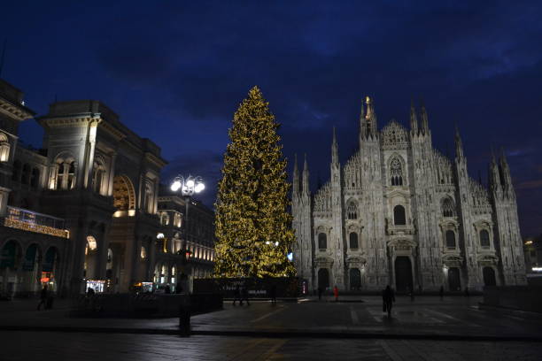 Milan Duomo square with the main Cathedral facade and decorated Christmas tree on blue sky background at dawn.