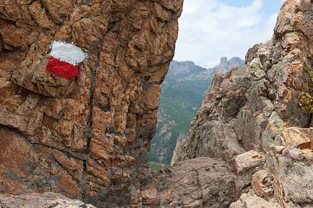 Crevice on the famous GR 20 hiking trail in Corsica. The white/red painting indicates the GR 20 trail. The crevice has to be passed. This image taken around 1 hour from Conca at a point called Bocca d'Usciolu. In the background part of the Bavella mountain range.