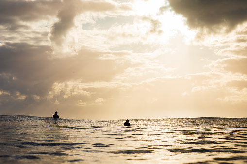 Person on surfboard with sunrise and dramatic light rays reflecting off the surface of the ocean in golden light.