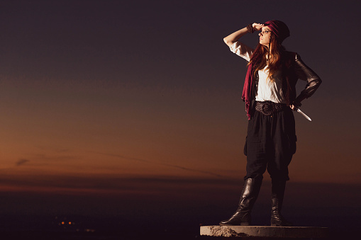 Outdoor portrait of young female in pirate costume, observing