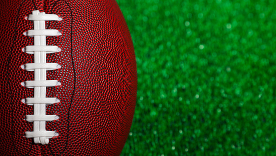 Close-up of the stringing of a brown american football ball over green grass.
