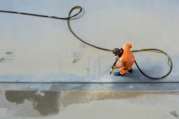 Sandblasting Man in orange workclothes sandblasting concrete surface with airpressure hose. Photographed from above. concrete work stock pictures, royalty-free photos & images