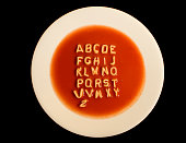 White bowl of soup with alphabet against black background