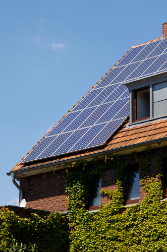 Solar panels on the roof of an older house covered with ivy.