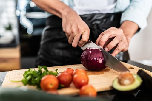 Close-up of man cutting red onion with a kitchen knife at home