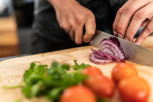 Close-up of man cutting red onion with a kitchen knife at home