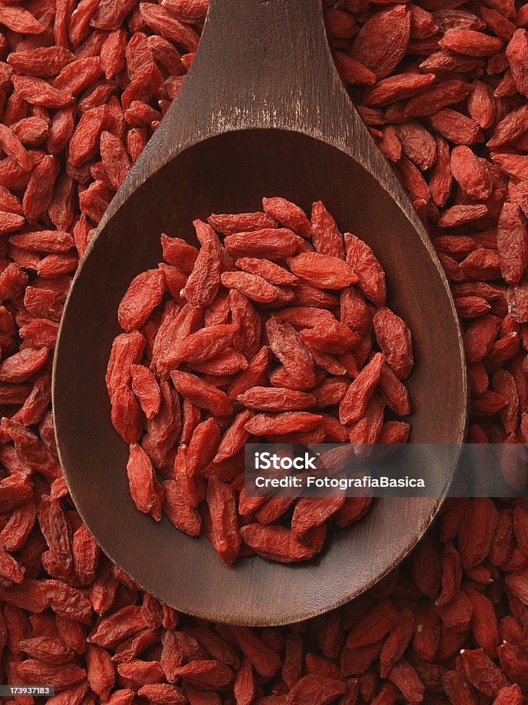 Top-view wooden spoon holding dried wolfberries A large, dark brown, wooden spoon that is filled with dried wolfberries.  Behind the spoon are  more wolfberries that fill up the background space of the image. Goji Berry Stock Photo