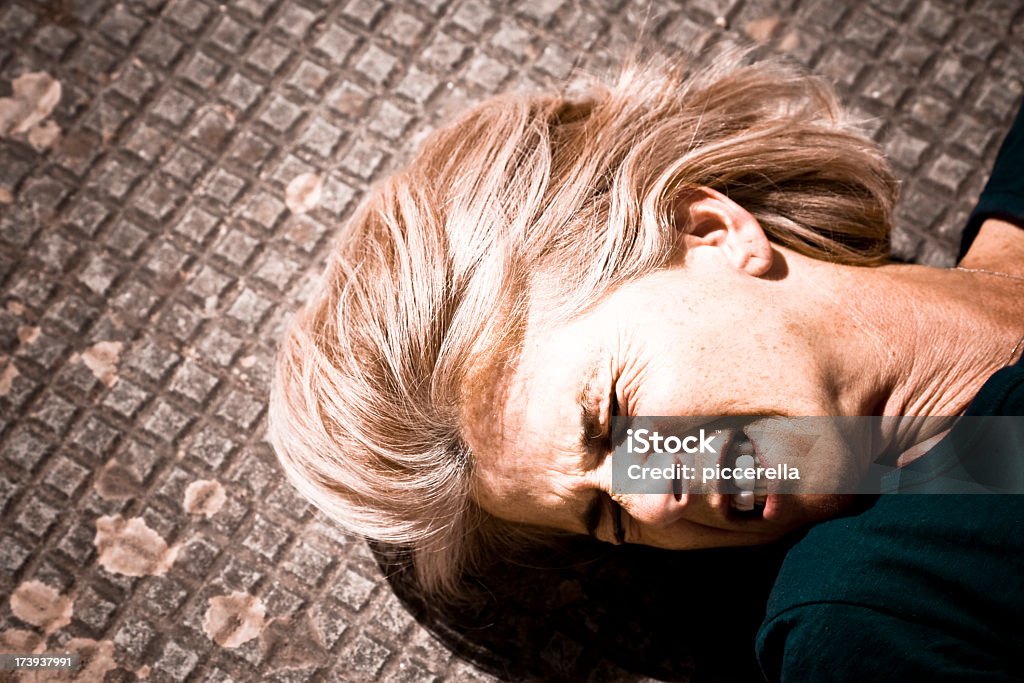 A woman lying in pain on a tile floor Suffering woman lying down on a concrete tiled floor, gritting her teeth. Epilepsy Stock Photo
