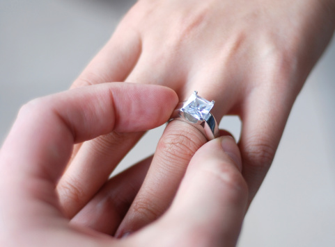Close up of a man placing a diamond engagement ring on a woman's finger.Wedding related images