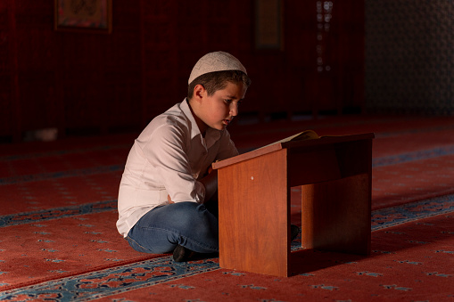 A boy reading the Qur'an in a mosque. A boy praying in a mosque. Sacred places for Muslims.