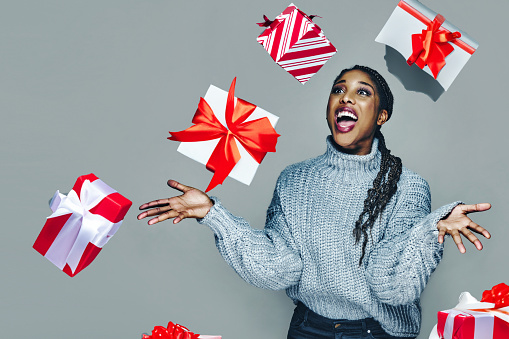Studio portrait of cheerful young woman with braided hair throwing red and white gift wrapped Christmas present mid air