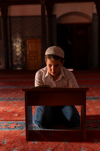 A boy reading the Qur'an in a mosque. A boy praying in a mosque. Sacred places for Muslims.