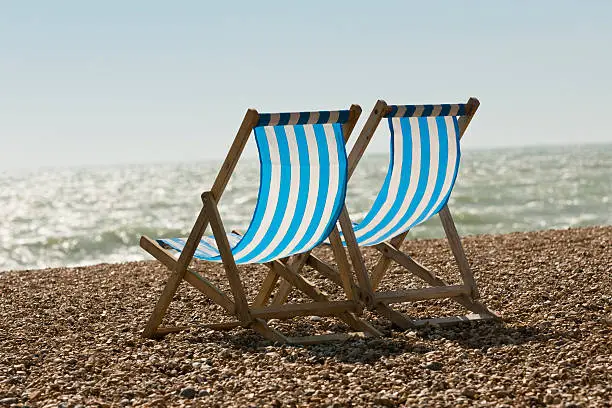 Two empty deckchairs on a sunny day at the beach.