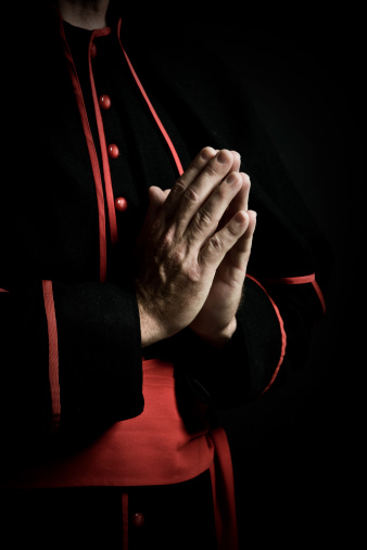 Priest holding a cross in his clasped hands during prayer.