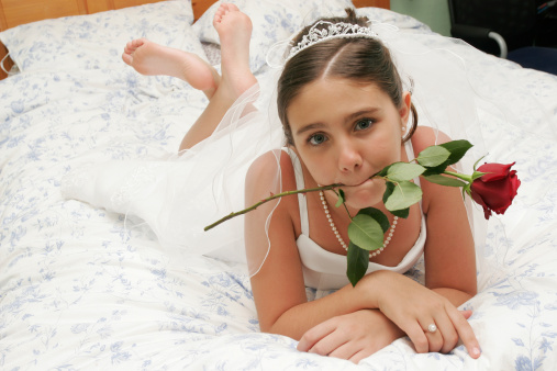 young girl biting a rose on a bed