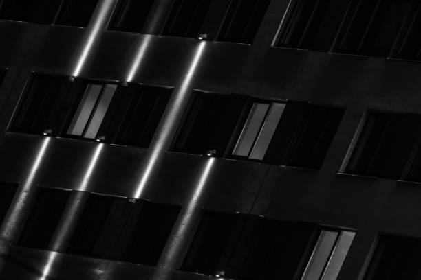 Dark facade at night with lines of illumination, abstract architecture background. Black and white photo