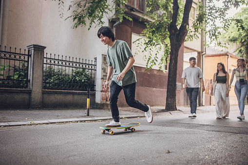 Young Asian man riding skateboard outdoors in city.