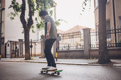 Young Asian man riding skateboard outdoors in city.