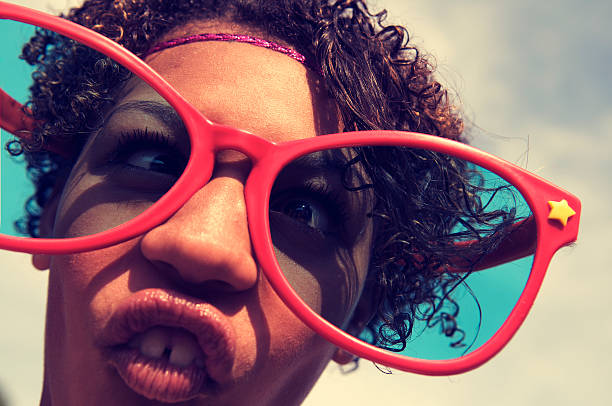 Teenage girl makes a goofy face behind oversize red sunglasses