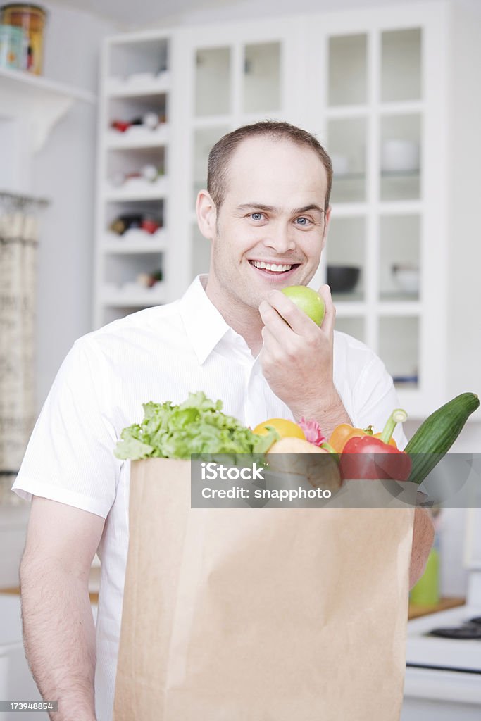 Groceries and Man in Kitchen eating Apple eating apple. Adult Stock Photo