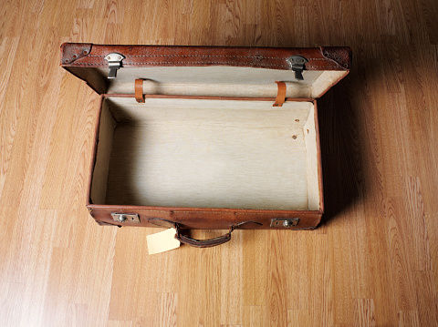 Empty old open leather suitcase with old luggage label, wooden floor, and copy space