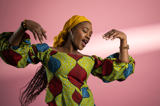 Beautiful young black woman dancing and singing in front of pink background.
