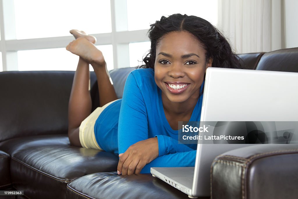 African-americanon female on sofa using laptop African descent female lying on sofa with laptop Adult Stock Photo