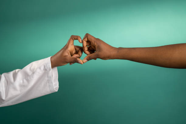 Two unrecognizable black women hands showing heart shape in front of green background.