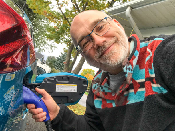 Selfie of mature man inserting electrical plug to charge his car during day of autumn