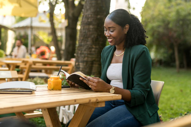 A young African American woman enjoys the gentle breeze of the cafe garden while engrossed in her book, creating the perfect blend of nature and literature